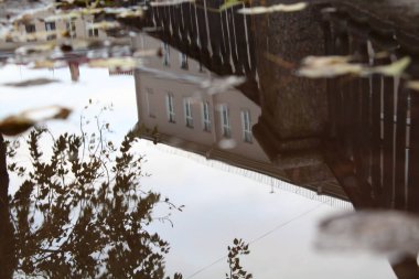 Sonbaharda granit dökme demir çitli kanal seti. Trotardaki su birikintilerinde yansıma