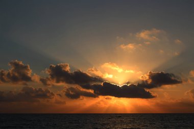 Mavi gökyüzünde beyaz bulutlar içinde denizin üzerinde güneş
