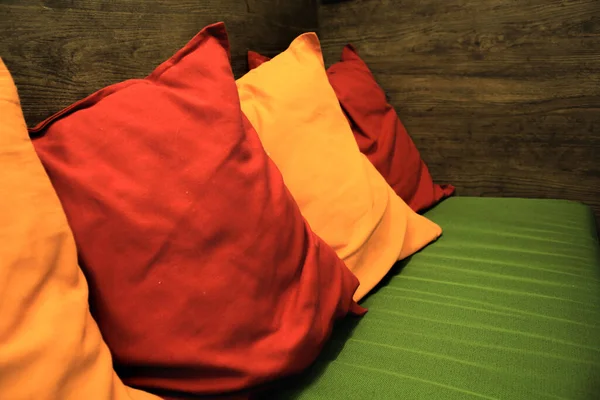 İlginç bir iç çözüm. Yeşil kanepede kırmızı ve sarı yastıklar ve ahşap bir duvar. Renk paleti, ayrıntı.