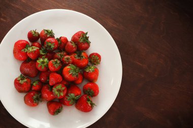 Ahşap bir arka planda beyaz bir tabakta çilek.