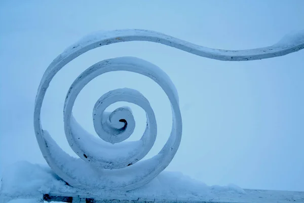 Spiral kıvrım. Kar altında bir park bankının metal süslemesi