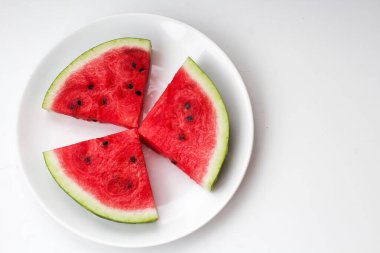 Beyaz bir tabakta üç dilim sulu olgun kırmızı karpuz.