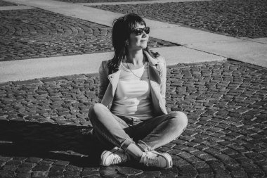 Kız kaldırımda nilüfer pozisyonunda oturuyor. Siyah beyaz fotoğraf.