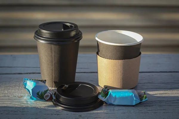 Açık bir günde tek kullanımlık fincanlarda kahve ve bir bankta şeker.