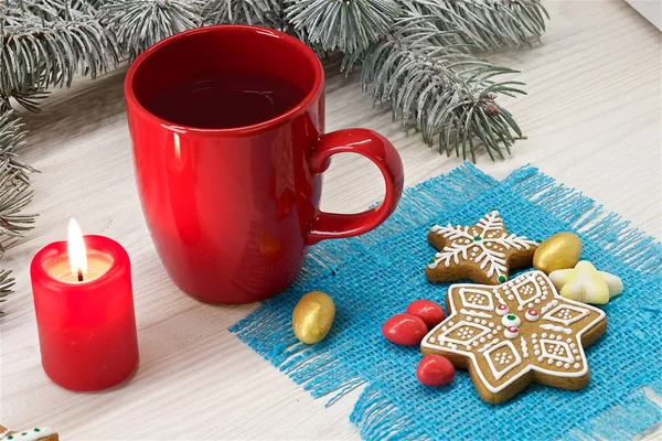 A cup of coffee,  a candle,  gingerbread and sweets on a light  wooden background with bly napkin and tree branches. Color photo