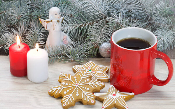 На белом деревянном фоне - группа пряников, чашка кофе, свечи и небольшие украшения. Цветное фото
.