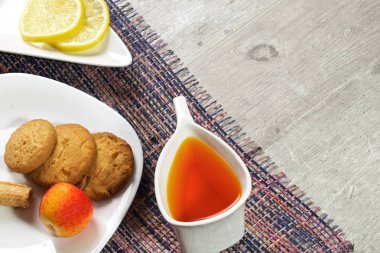 Açık ahşap bir arka planda çay, dekoratif bir çanak, ahşap bir fincan, çilek, tatlı kiraz, tatlılar, yoğurt, kurabiye ile orijinal bir kupa var.