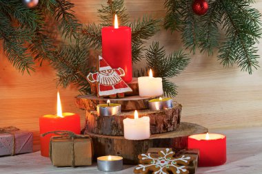 Hafif ahşap bir arka planda köknar dallarıyla Noel kurabiyeleri, hediyeler ve mumlar var..