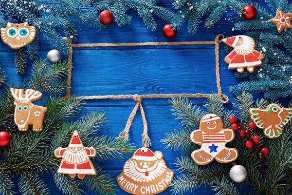 Christmas gingerbread cookies and gifts on a blue wooden background with decorations and branches of spruce.