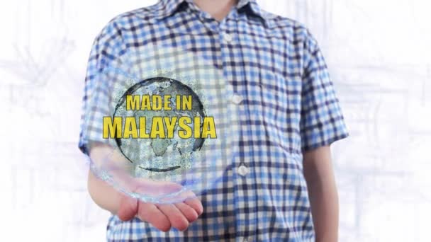 Young man shows a hologram of the planet Earth and text Made in Malaysia — Stock Video