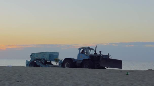 Um bulldozer grande com um reboque limpa a areia na praia no início da manhã — Vídeo de Stock