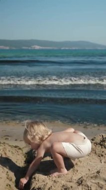 Küçük bir çocuk kumsaldaki yumuşak dalgalara kum atar, doğanın çarpıcı güzelliği arasında çocukluğun saf masumiyetini yakalar.