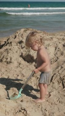 Güneşli bir kumsalın sıcak kumlarında elinde parlak renkli bir kürekle oynayan küçük bir çocuk çocukluk eğlencesi ve macerasını temsil ediyor.