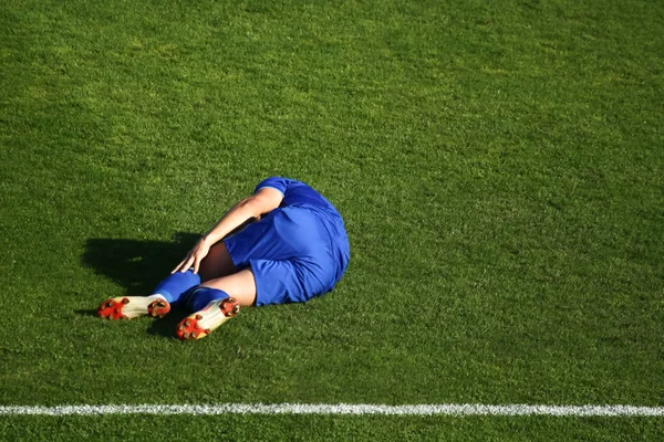 An injured football player laying down on the grass floor in pain and holds his leg.