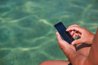 Sahil iskelede otururken Smartphone tutan bir adam.