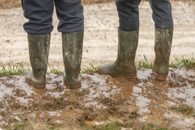 Two people in rubber boots standing in the mud. clipart