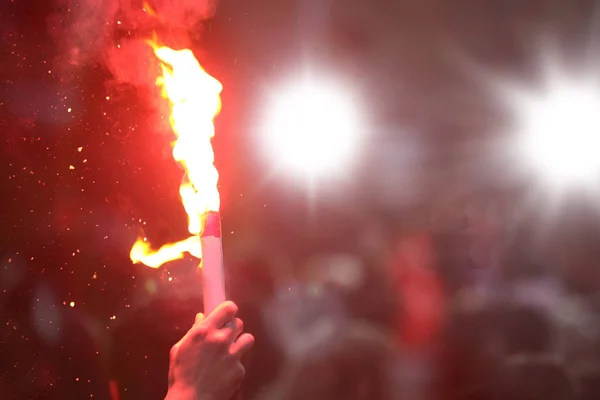 A hand holding a burning hand flare.