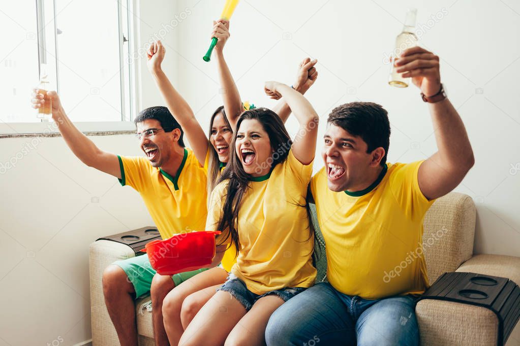 Group of friends watching soccer game on television, celebrating goal and screaming