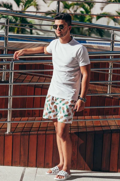 Portrait of young stylish man near the pool deck on sunny summer day. Lifestyle.