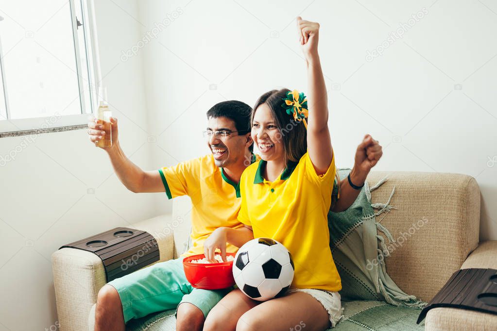 Couple watching soccer game on television, celebrating goal and screaming