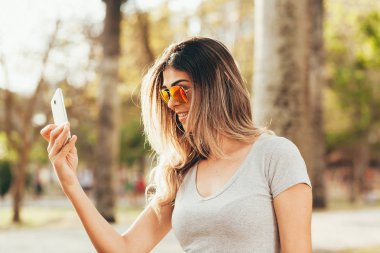 Gülümseyen kadın cep telefonuyla parkta güneşli bir günde