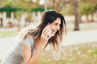 Gülümseyen kadın cep telefonuyla parkta güneşli bir günde