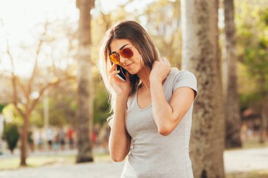 Gülümseyen kadın cep telefonuyla parkta güneşli bir günde