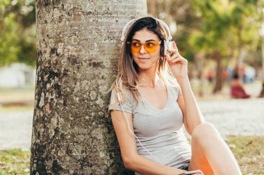 Güneşli bir günde kulaklıklar müzik dinlemek parkta genç kadın