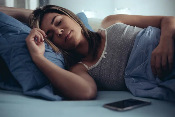 technology and people concept - young woman with smartphone sleeping in bed at home at night