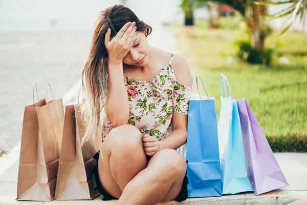 Sad young woman with shopping bags sitting on the sidewalk