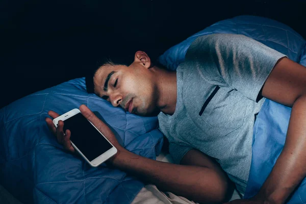 Man sleeping in bed and holding a mobile phone. Concept photo of smart phone addiction.