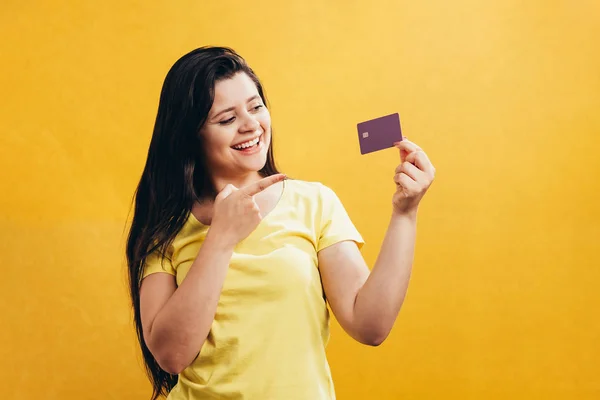 黄色の背景に分離されたプラスチック製のクレジット カードを示す幸せな若い女の子の肖像画 — ストック写真