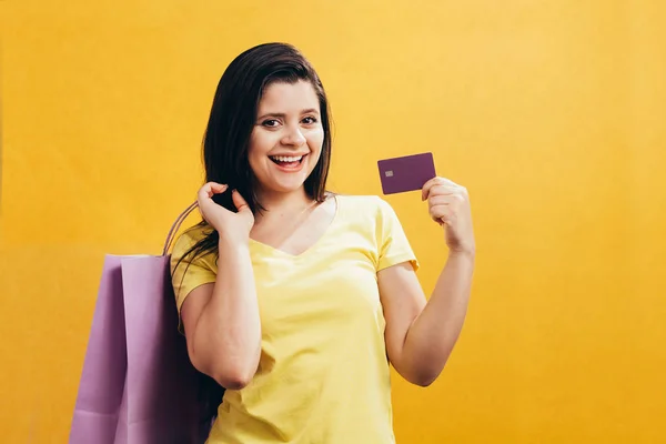 クレジット カードとショッピング バッグが黄色の背景上に分離されて幸せな女 — ストック写真