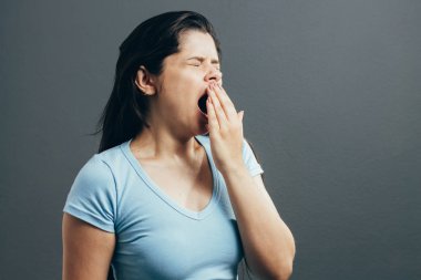 Genç kadın esneme. Gri arka plan üzerinde izole stüdyo portre.