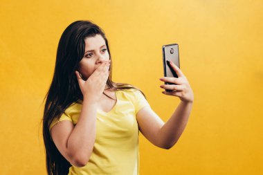 Sürpriz kadın Smartphone kullanarak sarı arka plan üzerinde izole