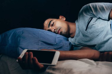 Yatakta uyuyan ve bir cep telefonu tutan adam. Konsept fotoğraf akıllı telefon bağımlılığı.