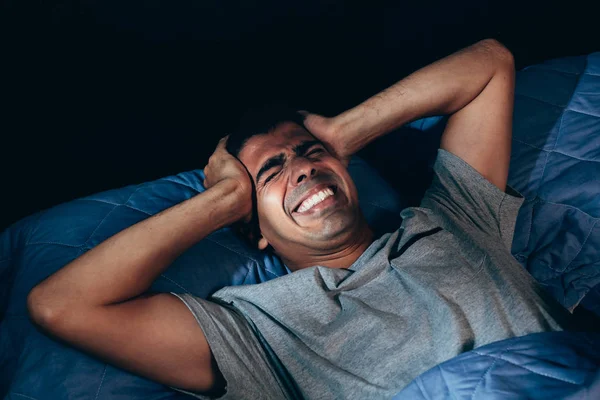 Handsome young man suffering from headache while lying in bed at night — Stock Photo, Image