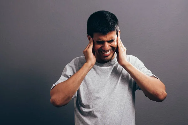 Oreille douloureuse. Concept de mal aux oreilles. Le triste homme qui pleure avec des maux de tête ou des douleurs sur fond gris. Expressions faciales et émotions des personnes concept . — Photo