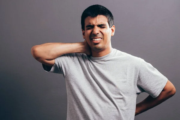 Portrét mladého muže s bolesti krku nad šedým pozadím — Stock fotografie