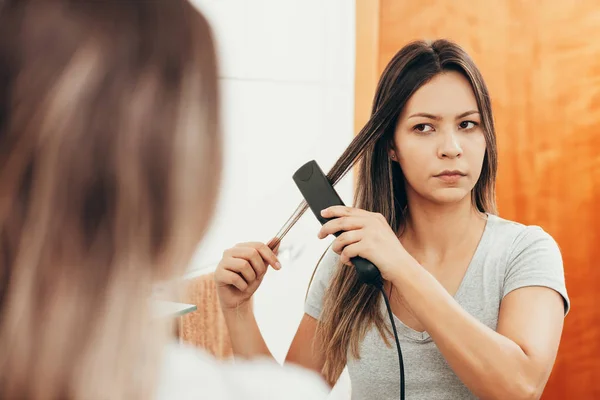 Genç Kadın Evde Saç Düzleştirici Ile Saç Düzleştirme — Stok fotoğraf