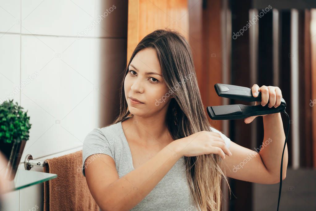 Young woman straightening hair with hair straightener at home