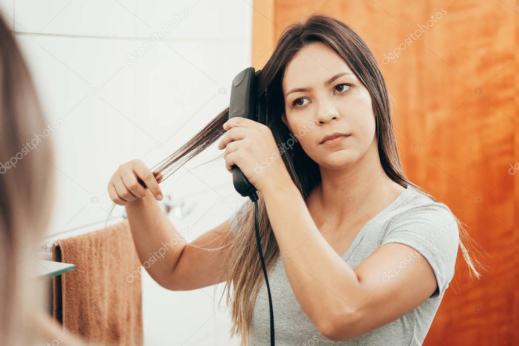 Young woman straightening hair with hair straightener at home