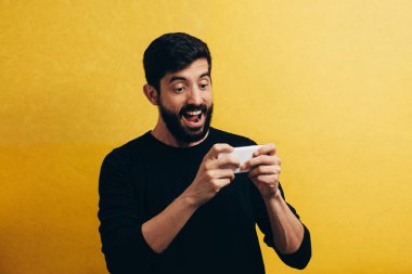 Sarı arka plan üzerinde izole cep telefonunda oyun oynamayı neşeli bir genç adam portresi