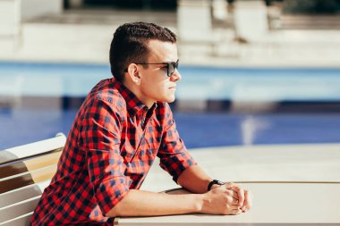 Havuz kenarında bir masada oturan rahat hipster adam portresi