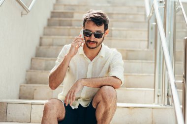 Telefonda konuşurken merdiven üzerinde oturan adam