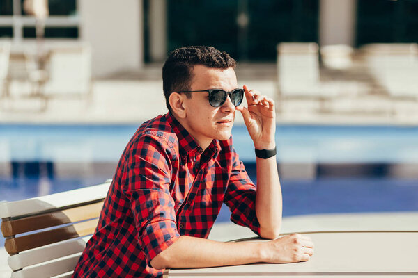 Portrait of relaxed hipster man sitting at a table near the pool