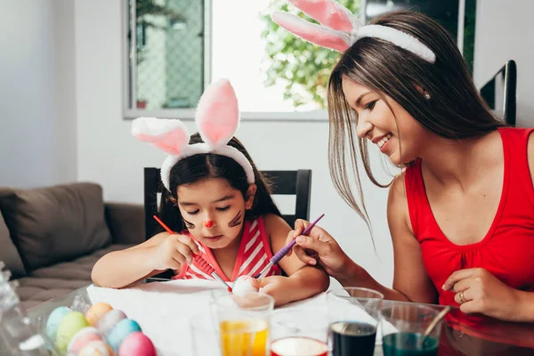 Vrolijk Pasen! Een moeder en haar dochter paaseieren schilderen. Gelukkige familie voorbereiden voor Pasen. Schattig klein kind meisje bunny oren dragen op Paasdag — Stockfoto