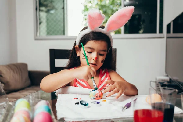 ¡Feliz Pascua! Una hermosa niña pintando huevos de Pascua. Familia feliz preparándose para la Pascua. Linda niña pequeña con orejas de conejo en el día de Pascua — Foto de Stock