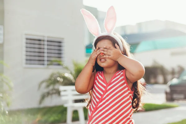 Милая маленькая девочка с кроличьими ушами и корзиной пасхальных яиц в саду. Охота на пасхальные яйца — стоковое фото