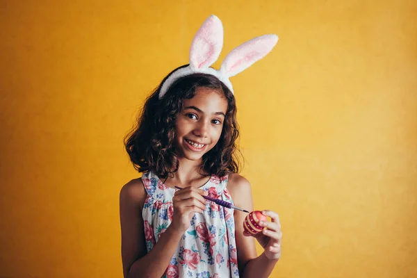 A happy girl painting Easter eggs over color background — Stock Photo, Image